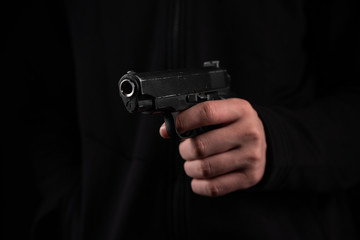 Gun in hand on black background. The threat of a firearm during a robbery on a dark street. Assault...