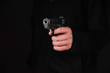Gun in hand on black background. The threat of a firearm during a robbery on a dark street. Assault with a semiautomatic weapon.
