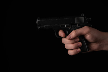 Gun in hand on black background. The threat of a firearm during a robbery on a dark street. Assault...