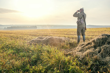 Hunting period, autumn season. Male with a gun looking in binoculars. Hunter man.