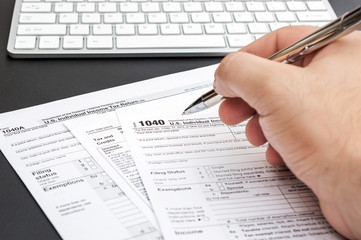 Man's hand filling tax form at workplace.