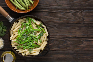 Penne pasta with green beans and cilantro on a wooden table. Tastier served with Parmesan