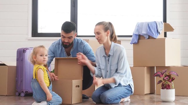 Kid wear denim overalls brought little moving box father. Family look into box. Background moving boxes, suit and flower in pot