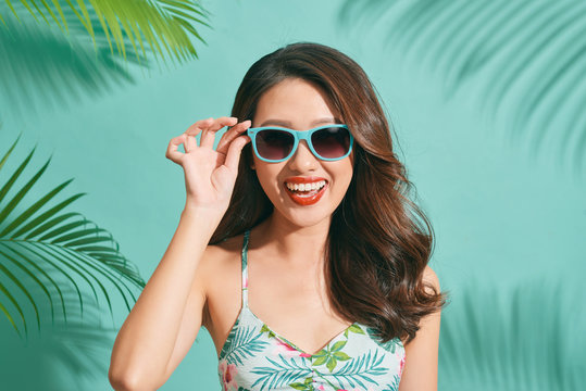 Asian young woman wearing a bikini and sunglasses having fun on blue background