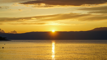 Fototapeta premium Yellow-orange sunset on the Adriatic. The sun is hiding behind the mountains of Istria