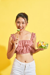 Young woman eating a vegetable salad on yellow background
