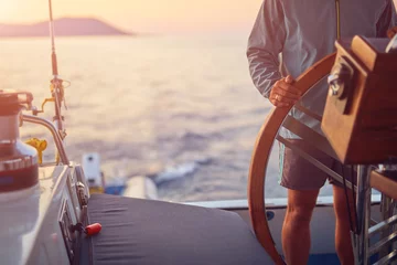 Fototapeten Sailor using wheel to steer rudder on a sailing boat. © astrosystem