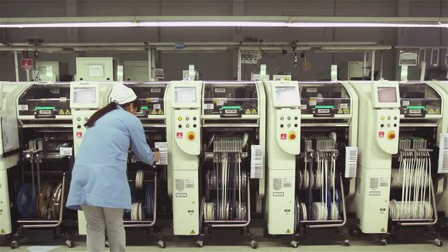 Female Worker in the PCB Assembly Plant, Checking a Checking a Chip Mounter SMT Placement Machine.