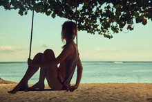 Young woman swinging on a sandy tropical beach.