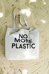 Eco bag with No More Plastic concept sign on topical beach sand, top view