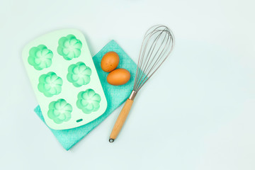 Kitchen utensils and baking accessories on blue background with copy space. Potholder, whisk, silicone cupcake baking dish and eggs for cooking any recipes. Set for mock ups and bakery design.