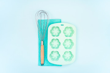 Fototapeta na wymiar Baking accessories and kitchen utensils and on blue background with copy space. Potholder, whisk and silicone cupcake baking dish for cooking any recipes. Set for mock ups and bakery design. Flat lay.
