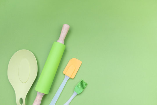 Kitchen silicone utensils for baking and cooking any dishes. Rolling pin, spatula and culinary brush on green background with copy space. Flat lay.