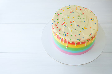 Cake blank with colorful rainbow cream on a white background decorated with colorful sprinkles, poured with chocolate. Simple minimalism. Top view.