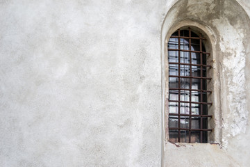 Medieval arched window with rusty grating on a light wall