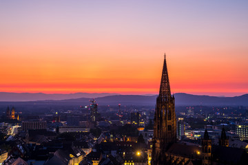 Germany, Intensive red sky sunset over muenster church steeple and skyline of city freiburg im breisgau in summer surrounded by black forest