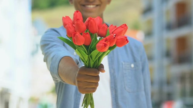 Positive man giving flowers into camera, delivery of bouquets, romantic present