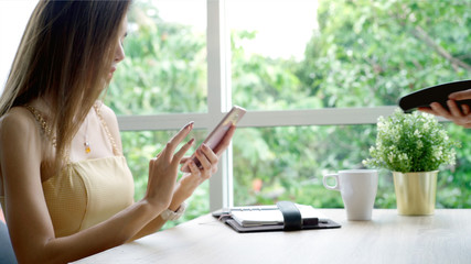 Young beautiful Asian woman enjoying a relaxing moment working and using mobile phone as mobile smart payment to pay for a coffee in the coffeeshop on a bright sunny day