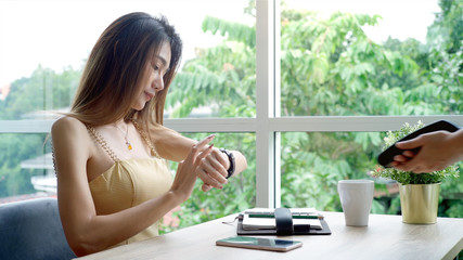 Young beautiful Asian woman enjoying a relaxing moment working and using mobile phone as mobile smart payment to pay for a coffee in the coffeeshop on a bright sunny day