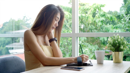Obraz premium Young beautiful Asian woman enjoying a relaxing moment working and using mobile phone as mobile smart payment to pay for a coffee in the coffeeshop on a bright sunny day
