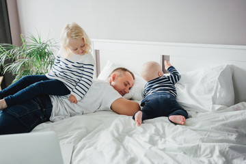 Young happy father lying on bed while his daughter play with him. Tired father sleep but his...