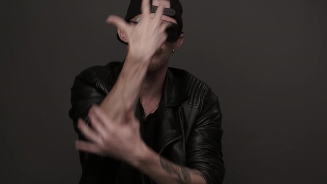 Portrait of a tough guy in a black leather jacket. Stylish man in glasses emotionally dancing. Caucasian man dancing in studio. Contemporary dance. Krump. Hip hop style, listening to music. Closeup