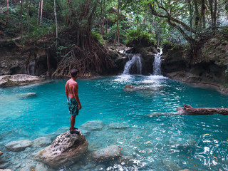 Fit man alone on the bamboo raft in front of the waterfall with turquoise water in Kawasan Falls in Cebu Island, Philippines