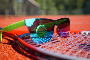 Sunglasses and ball on a tennis racket