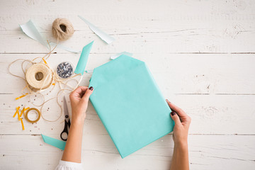 Top view on gift wrapping. The girl packs a gift in a paper of turquoise color. Gift ribbons,...