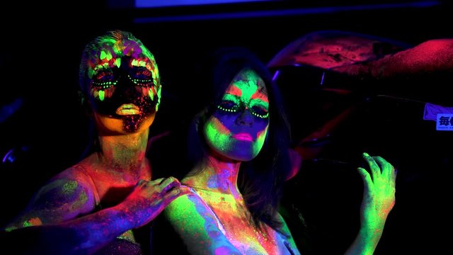 Two girls with futuristic fluorescent bodyart in ultraviolet light in night club