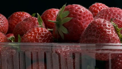 Rotation of juicy ripe strawberries in disposable plastic pack on black background. Rotation 360 degrees, closeup. 4K - 50fps  