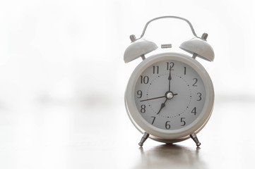 Alarm clock on wooden table for wake up time with light from window, selective focus