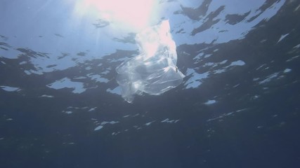 Plastic pollution, Transparent plastic bag in bue water. Discarded plastic bag slowly drifting under surface of blue water near reef in sunray. Transparent plastic bag floats in Mediterranean Sea 