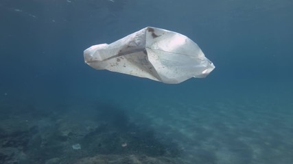  Plastic pollution, White plastic bag in bue water. Slow motion, discarded plastic bag slowly drifting under surface of blue water in sunray. White plastic bag floats in Mediterranean Sea, Europe. 