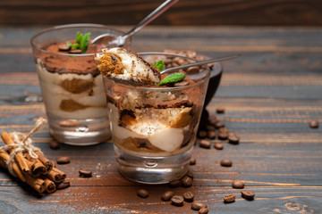 Portion of Classic tiramisu dessert in a glass and savoiardi cookies on wooden background