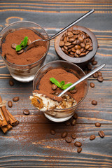 Portion of Classic tiramisu dessert in a glass and savoiardi cookies on wooden background