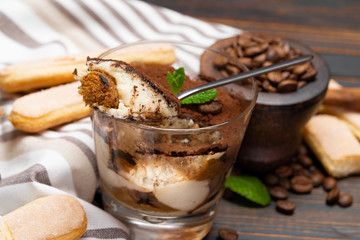 Portion of Classic tiramisu dessert in a glass and savoiardi cookies on wooden background