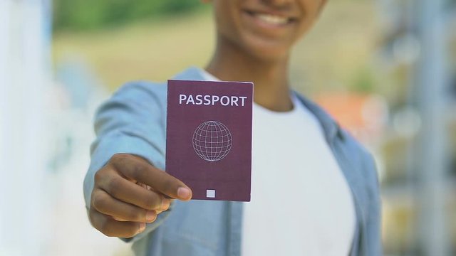 Afro-american man holding red passport, migration policy, simplified visa regime