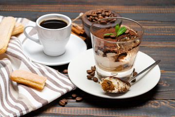 Portion of Classic tiramisu dessert in a glass, cup of coffee and savoiardi cookies on wooden background