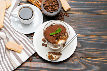 Portion of Classic tiramisu dessert in a glass, cup of coffee and savoiardi cookies on wooden background