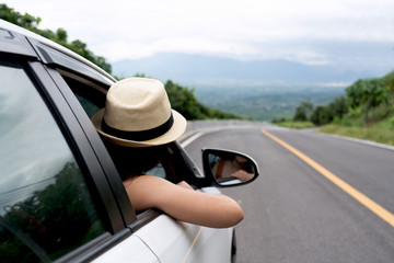 Relaxed happy traveler, Young beautiful girl wearing white hat weave Reach out of the car at sunshine and nature view with mountain road background