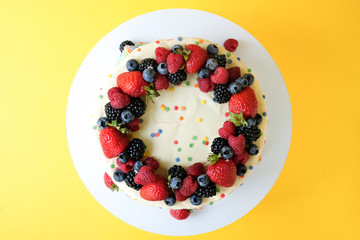 Cake on birthday with colorful rainbow cream on a yellow background decorated with berries, colorful sprinkles, poured with chocolate. Top view.