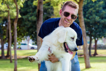 Man with his dog playing outdoor in the park. Young owner hugs his pet.