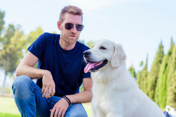 Man with his dog playing outdoor in the park. Young owner hugs his pet.