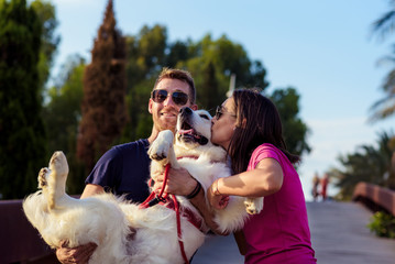 Beautiful romantic couple is having fun with their dog labrador retriever outdoors. Couple of guys playing with their dog on the park.Portrait of happy young couple hugging and kissing their dog