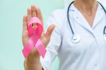 Pink ribbon for breast cancer awareness in doctor's hand, women breast tumor illness campaign.
