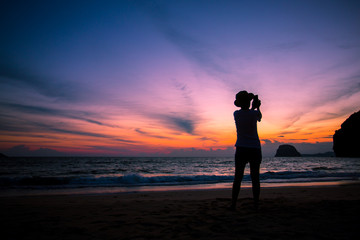 Fototapeta premium Silhouette of The girl is walking happily Use the phone at the beach during the sunset and her enjoying freedom feeling happy at sunset 