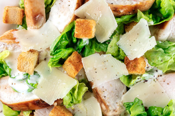 Caesar salad texture. Slices of chicken breast, green lettuce, Parmesan cheese, and croutons, shot from the top with the typical dressing