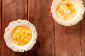 Tortellini with broth and cream sauce, Italian food, shot from the top on a dark rustic wooden background with copy space