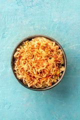 Instant soba noodles with carrot and a sauce, overhead shot on a teal blue background with copyspace